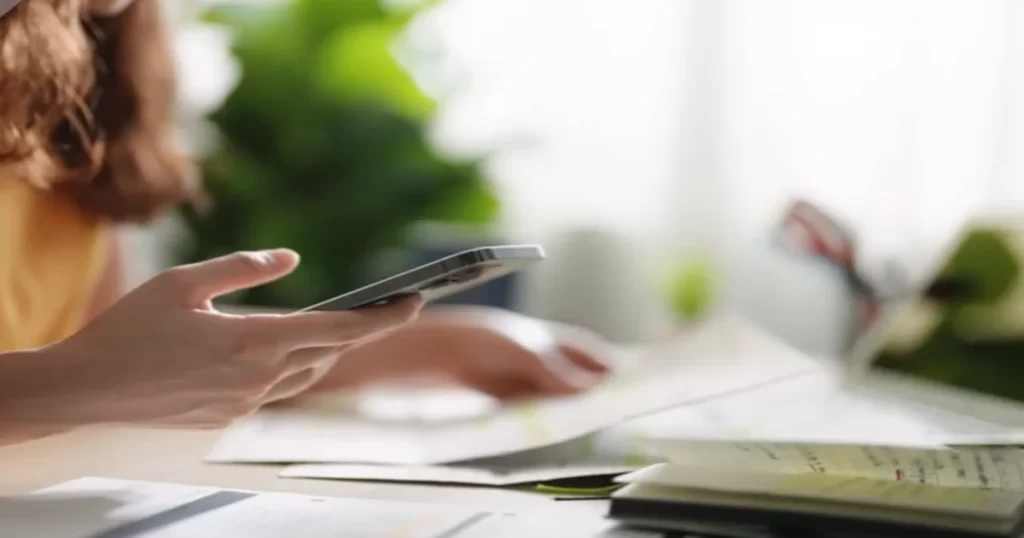 Donna tuo smartphone in mano sulla scrivania con documenti di prestiti Online