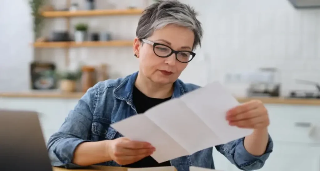 donna matura seria in occhiali che legge il conto in cucina.